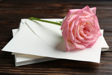 Photo of Stack of love letters and beautiful rose on wooden table, closeup