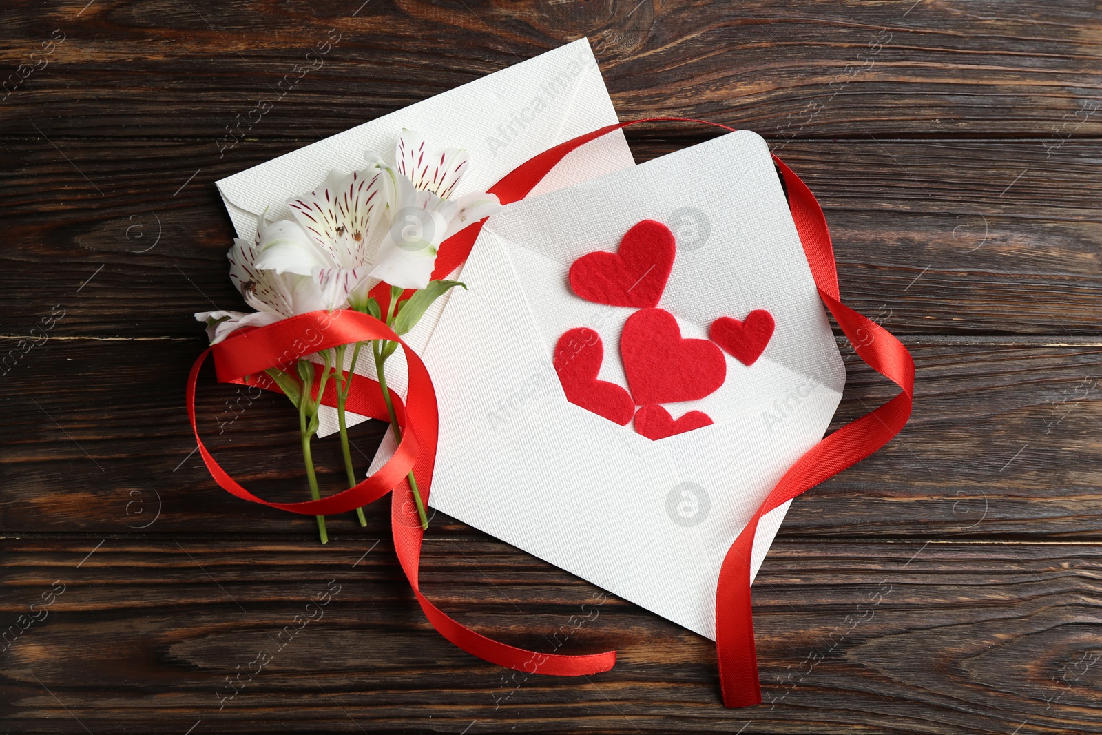 Love letters, red hearts, ribbon and beautiful lilies on wooden table, flat lay Photo of Love letters, red hearts, ribbon and beautiful lilies on wooden table, flat lay