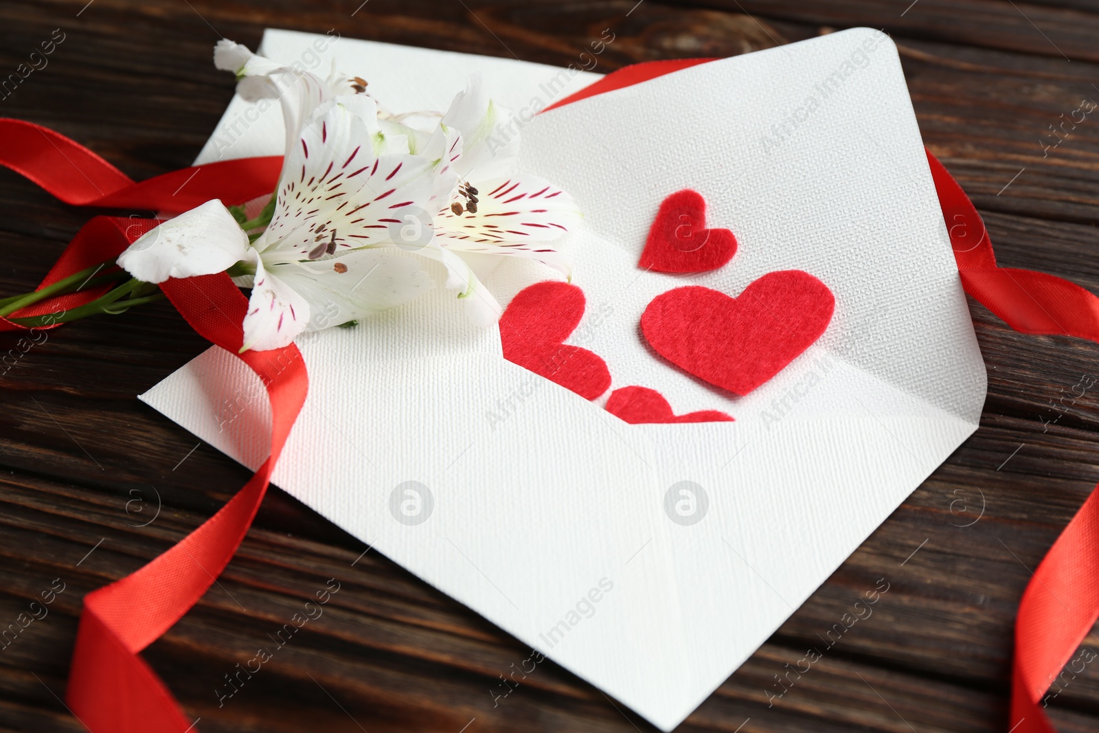 Love letters, red hearts, ribbon and beautiful lilies on wooden table, closeup Photo of Love letters, red hearts, ribbon and beautiful lilies on wooden table, closeup