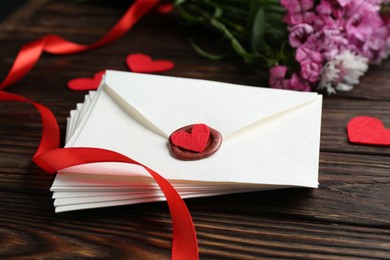 Photo of Stack of love letters, red hearts and beautiful flowers on wooden table, closeup