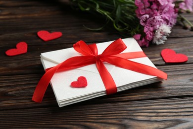 Photo of Stack of love letters, red hearts and beautiful flowers on wooden table, closeup
