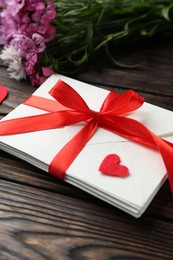Photo of Stack of love letters, red hearts and beautiful flowers on wooden table, closeup