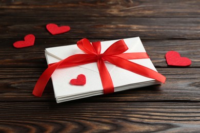 Photo of Stack of love letters and red hearts on wooden table, closeup