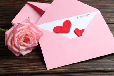 Photo of Love letter, envelopes, beautiful rose and red hearts on wooden table, closeup