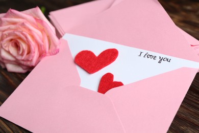 Photo of Love letter, envelopes, beautiful rose and red hearts on wooden table, closeup