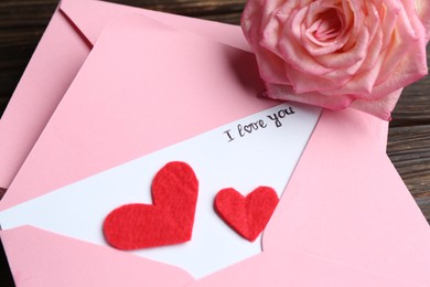 Photo of Love letter, envelopes, beautiful rose and red hearts on table, above view