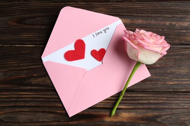 Photo of Love letter, envelope, beautiful rose and red hearts on wooden table, top view