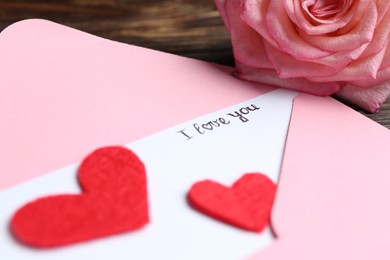 Photo of Love letter, envelope, beautiful rose and red hearts on table, closeup