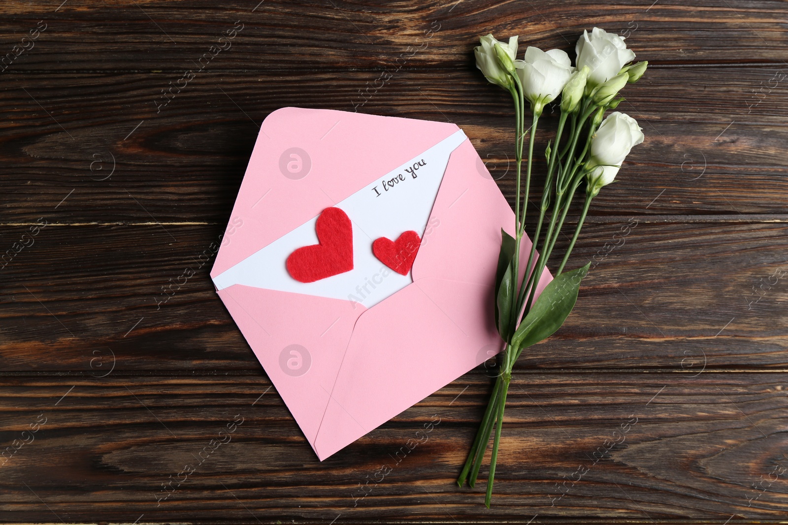 Love letter, envelope, beautiful flowers and red hearts on wooden table, flat lay Photo of Love letter, envelope, beautiful flowers and red hearts on wooden table, flat lay
