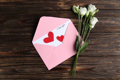Photo of Love letter, envelope, beautiful flowers and red hearts on wooden table, flat lay