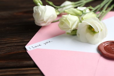 Photo of Letter with phrase I Love You, envelope and beautiful flowers on wooden table, closeup