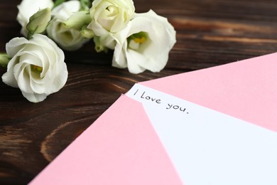 Photo of Letter with phrase I Love You, envelope and beautiful flowers on wooden table, closeup
