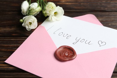 Photo of Letter with phrase I Love You, envelope and beautiful flowers on wooden table, closeup