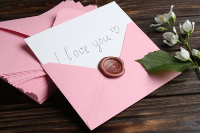Photo of Letter with phrase I Love You, envelopes and beautiful flowers on wooden table, closeup