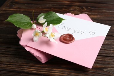 Photo of Letter with phrase I Love You, envelopes and beautiful flowers on wooden table, closeup