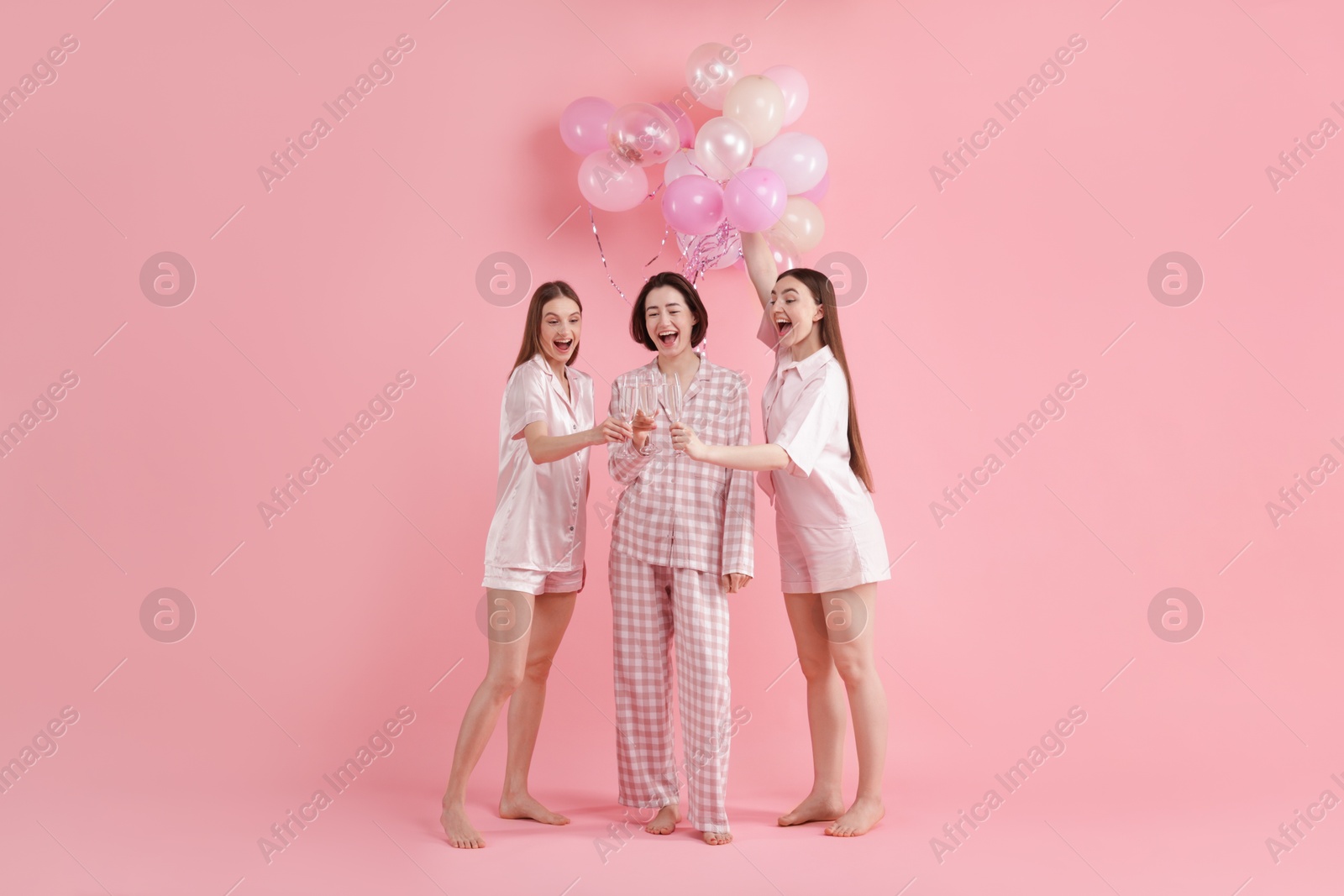 Photo of Pajama party. Happy friends with balloons clinking glasses on pink background