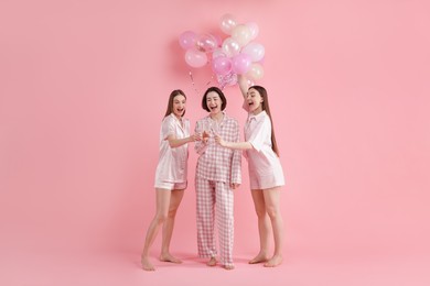 Photo of Pajama party. Happy friends with balloons clinking glasses on pink background