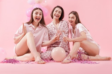 Photo of Pajama party. Happy friends with balloons and tinsel clinking glasses on pink background
