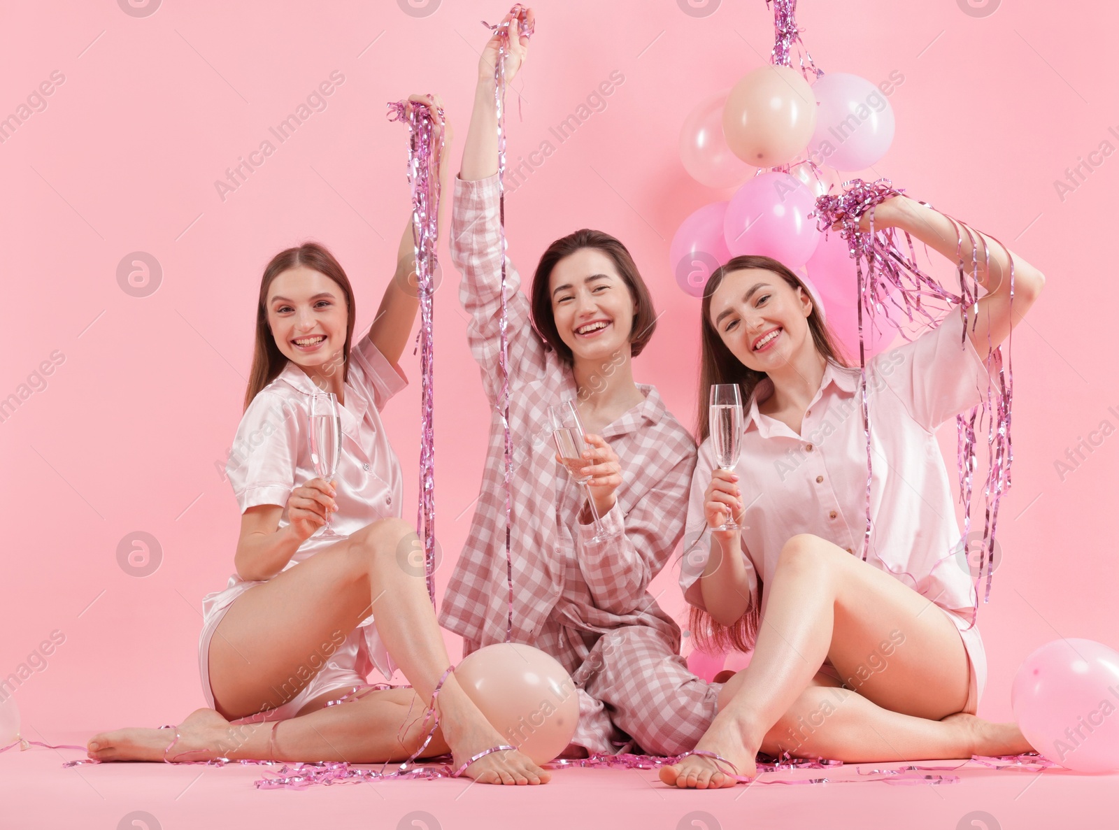 Pajama party. Happy friends with glasses, balloons and tinsel on pink background Photo of Pajama party. Happy friends with glasses, balloons and tinsel on pink background