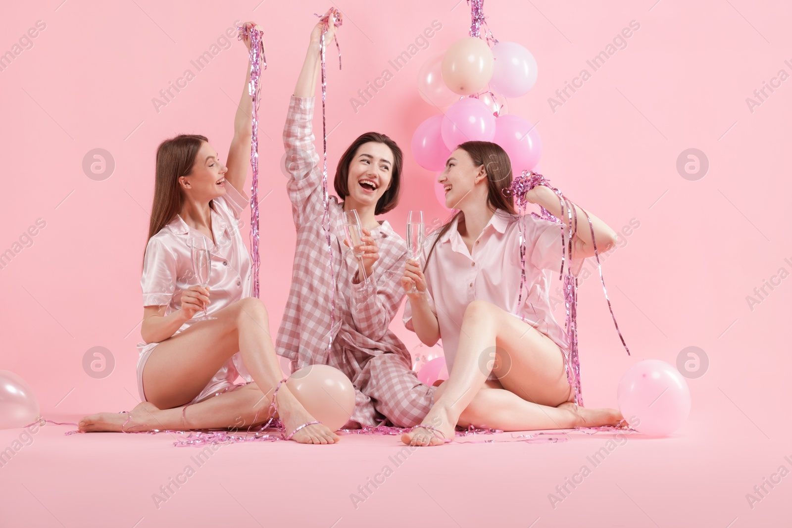 Pajama party. Happy friends with glasses, balloons and tinsel on pink background Photo of Pajama party. Happy friends with glasses, balloons and tinsel on pink background