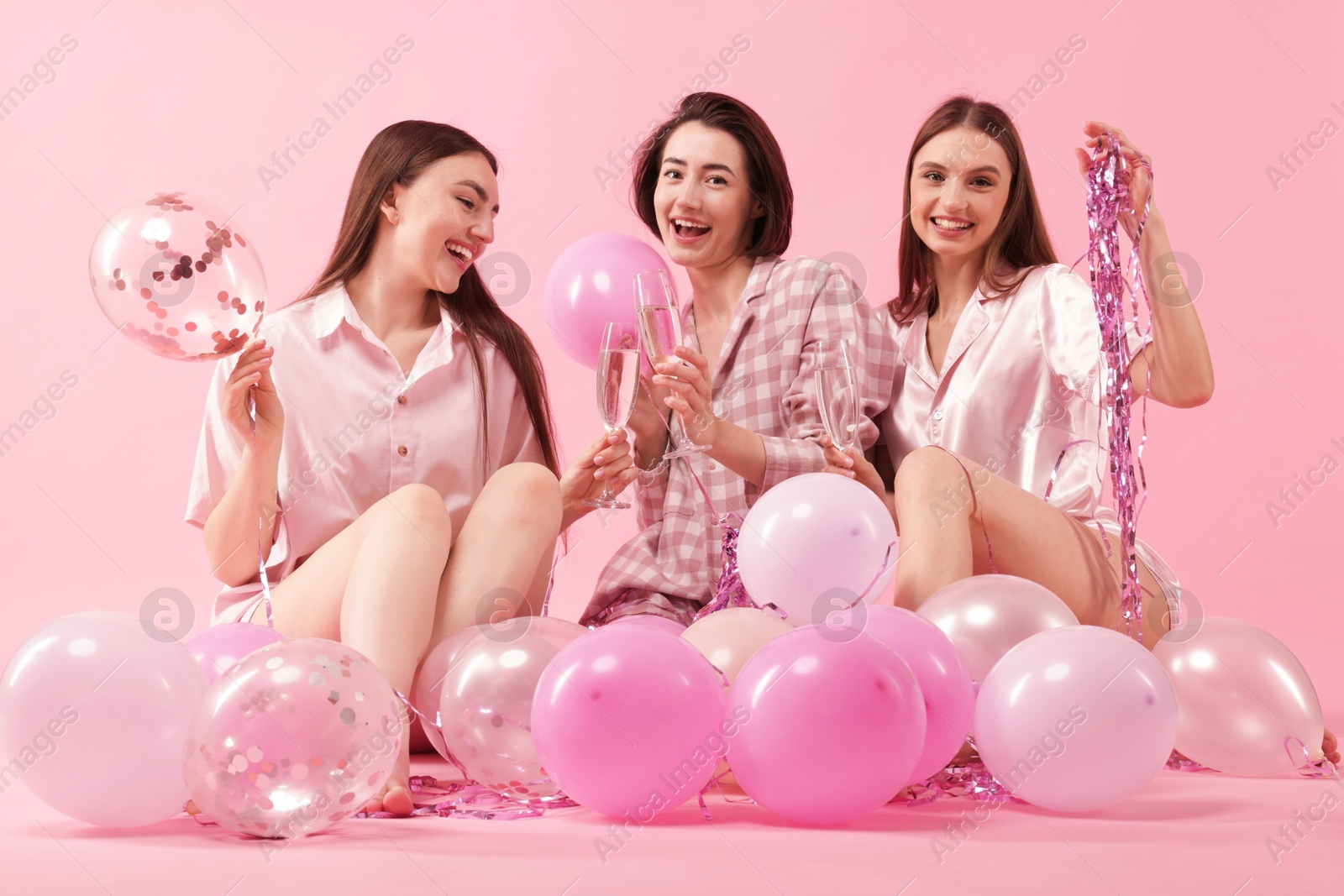Pajama party. Happy friends with glasses, balloons and tinsel on pink background Photo of Pajama party. Happy friends with glasses, balloons and tinsel on pink background