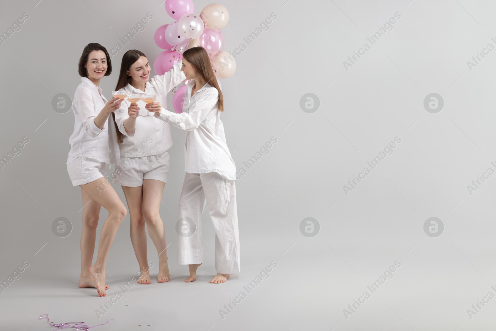 Pajama party. Happy friends with balloons clinking glasses on grey background. Space for text Photo of Pajama party. Happy friends with balloons clinking glasses on grey background. Space for text