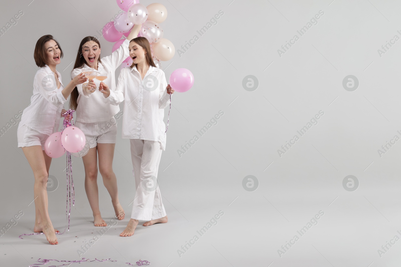 Pajama party. Happy friends with balloons clinking glasses on grey background. Space for text Photo of Pajama party. Happy friends with balloons clinking glasses on grey background. Space for text