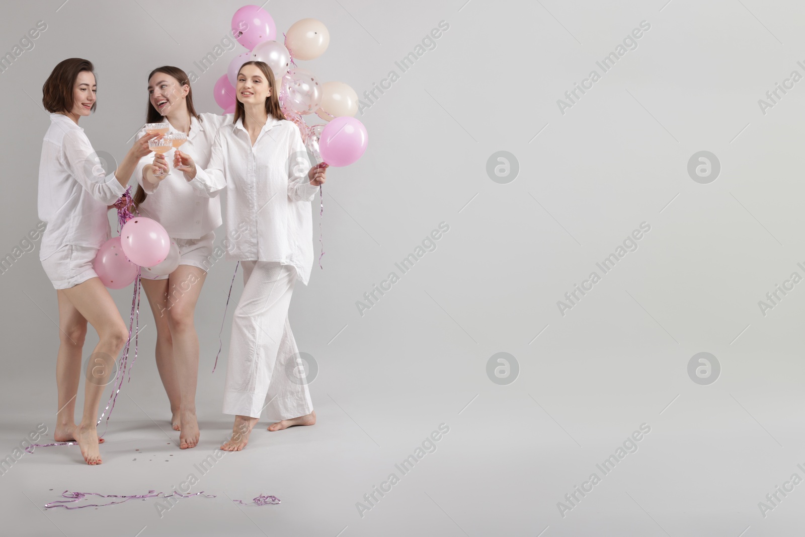 Pajama party. Happy friends with balloons clinking glasses on grey background. Space for text Photo of Pajama party. Happy friends with balloons clinking glasses on grey background. Space for text