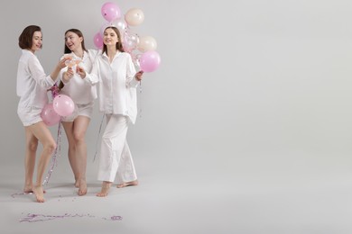 Photo of Pajama party. Happy friends with balloons clinking glasses on grey background. Space for text