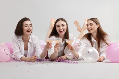 Photo of Pajama party. Happy friends with tinsel and balloons clinking glasses on grey background