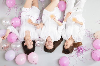 Photo of Pajama party. Happy friends with glasses of alcoholic drink, balloons and tinsel on grey background, top view