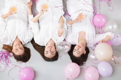 Photo of Pajama party. Happy friends with glasses of alcoholic drink, balloons and tinsel on grey background, top view