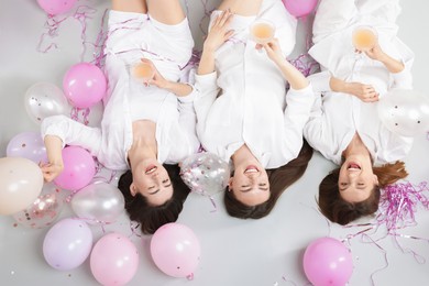 Photo of Pajama party. Happy friends with glasses of alcoholic drink, balloons and tinsel on grey background, top view