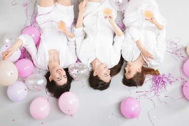 Photo of Pajama party. Happy friends with glasses of alcoholic drink, balloons and tinsel on grey background, top view