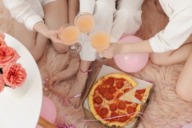 Photo of Pajama day. Friends with glasses of alcoholic drink and pizza on faux fur, above view