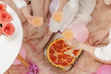 Photo of Pajama day. Friends with glasses of alcoholic drink and pizza on faux fur, above view
