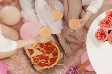 Photo of Pajama day. Friends with glasses of alcoholic drink and pizza on faux fur, above view