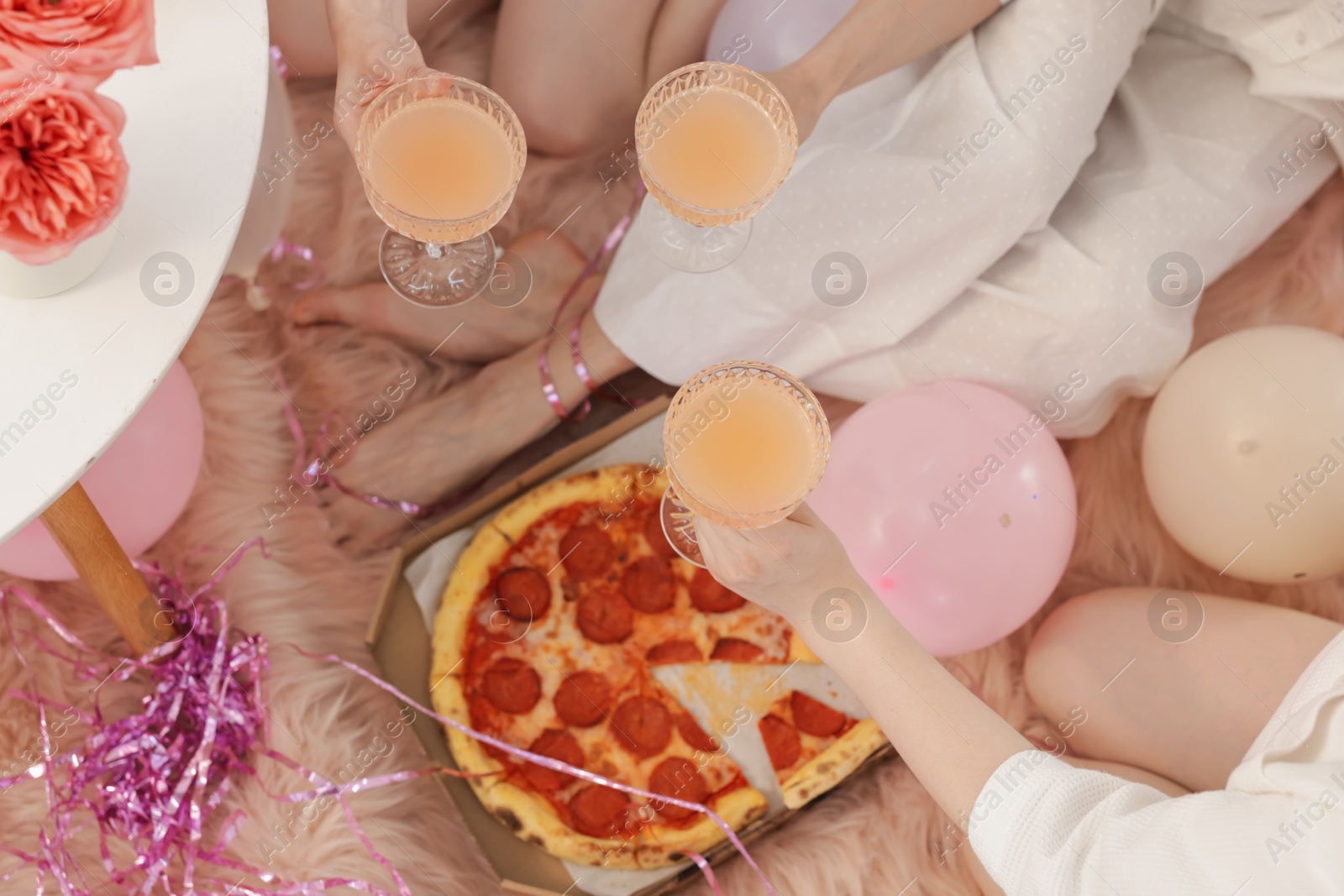 Photo of Pajama day. Friends with glasses of alcoholic drink and pizza on faux fur, above view