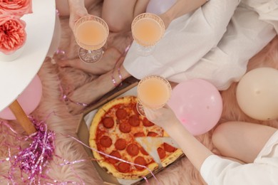 Photo of Pajama day. Friends with glasses of alcoholic drink and pizza on faux fur, above view
