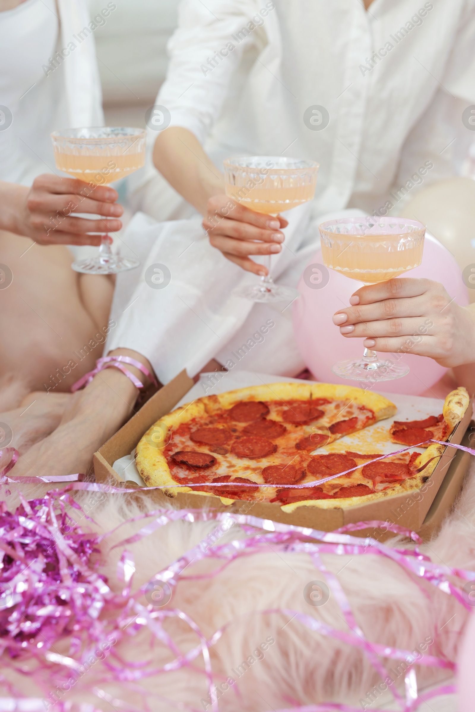 Pajama day. Friends with glasses of alcoholic drink and pizza on faux fur, closeup Photo of Pajama day. Friends with glasses of alcoholic drink and pizza on faux fur, closeup