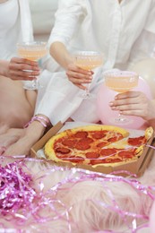 Photo of Pajama day. Friends with glasses of alcoholic drink and pizza on faux fur, closeup