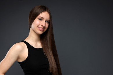 Photo of Portrait of smiling teenage girl with healthy long hair on dark grey background. Space for text