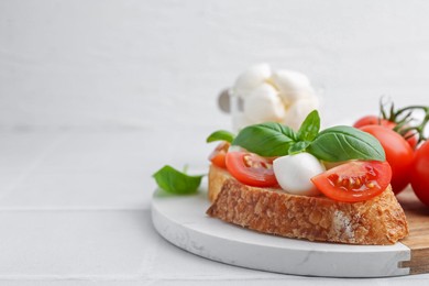 Photo of Tasty sandwich with mozzarella cheese, tomatoes and basil on light tiled table, closeup. Space for text