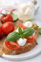 Photo of Tasty sandwich with mozzarella cheese, tomatoes and basil on light table, closeup