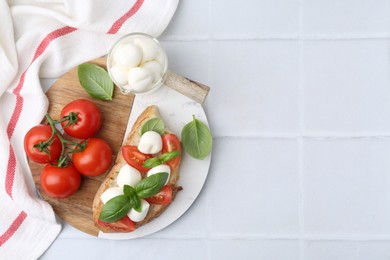 Photo of Tasty sandwich with mozzarella cheese, tomatoes and basil on light tiled table, top view. Space for text