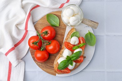 Photo of Tasty sandwich with mozzarella cheese, tomatoes and basil on light tiled table, top view