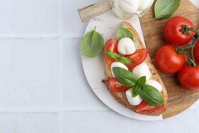 Photo of Tasty sandwich with mozzarella cheese, tomatoes and basil on light tiled table, top view. Space for text