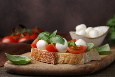 Photo of Tasty sandwich with mozzarella cheese, tomatoes and basil on wooden table against brown background, closeup