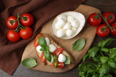 Photo of Tasty sandwich with mozzarella cheese, tomatoes and basil on wooden table, flat lay