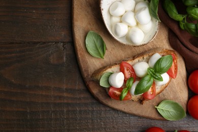 Photo of Tasty sandwich with mozzarella cheese, tomatoes and basil on wooden table, flat lay. Space for text